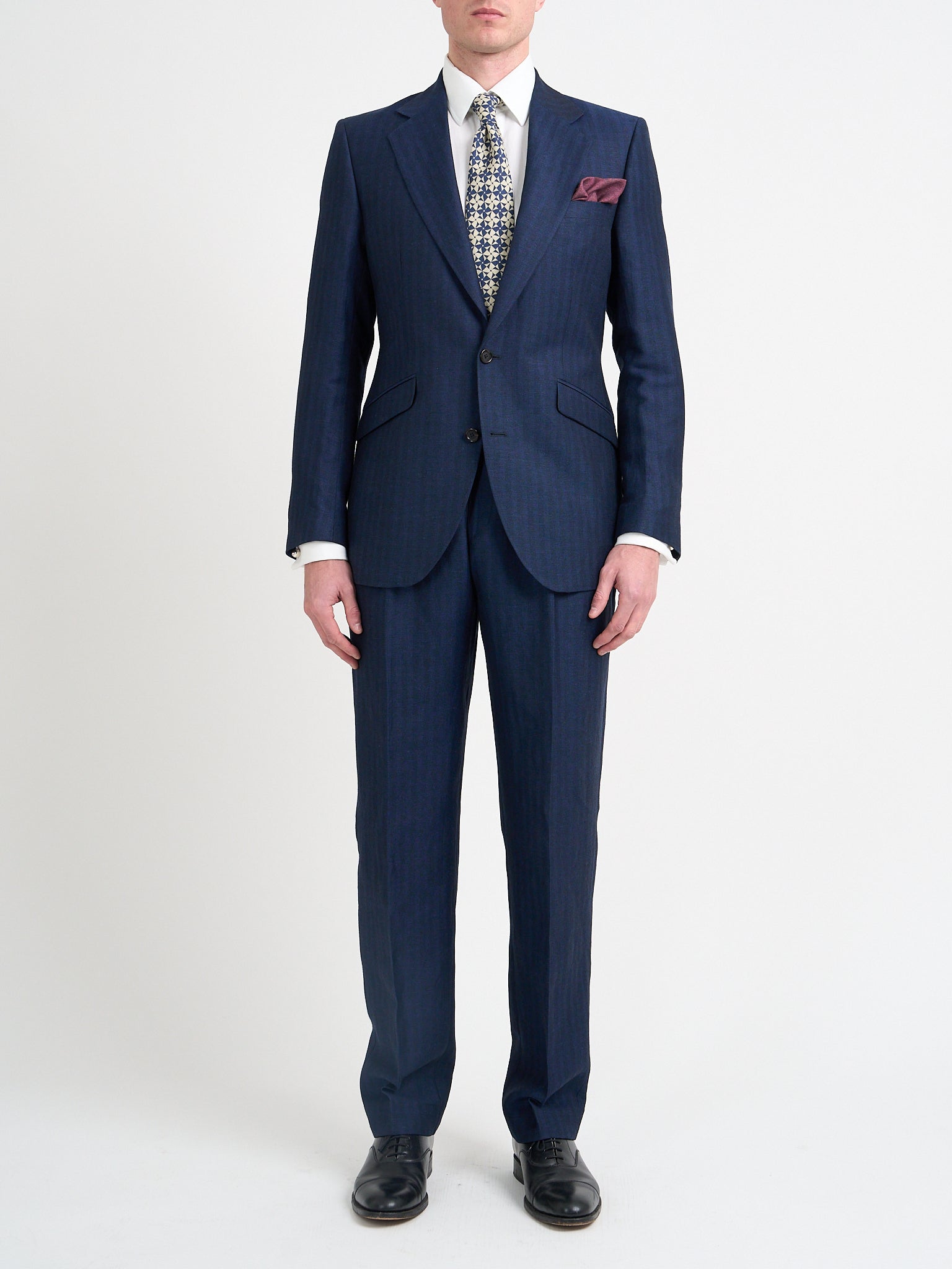 A navy herringbone unlined suit in a wool and linen mix, shown on a model from the front.