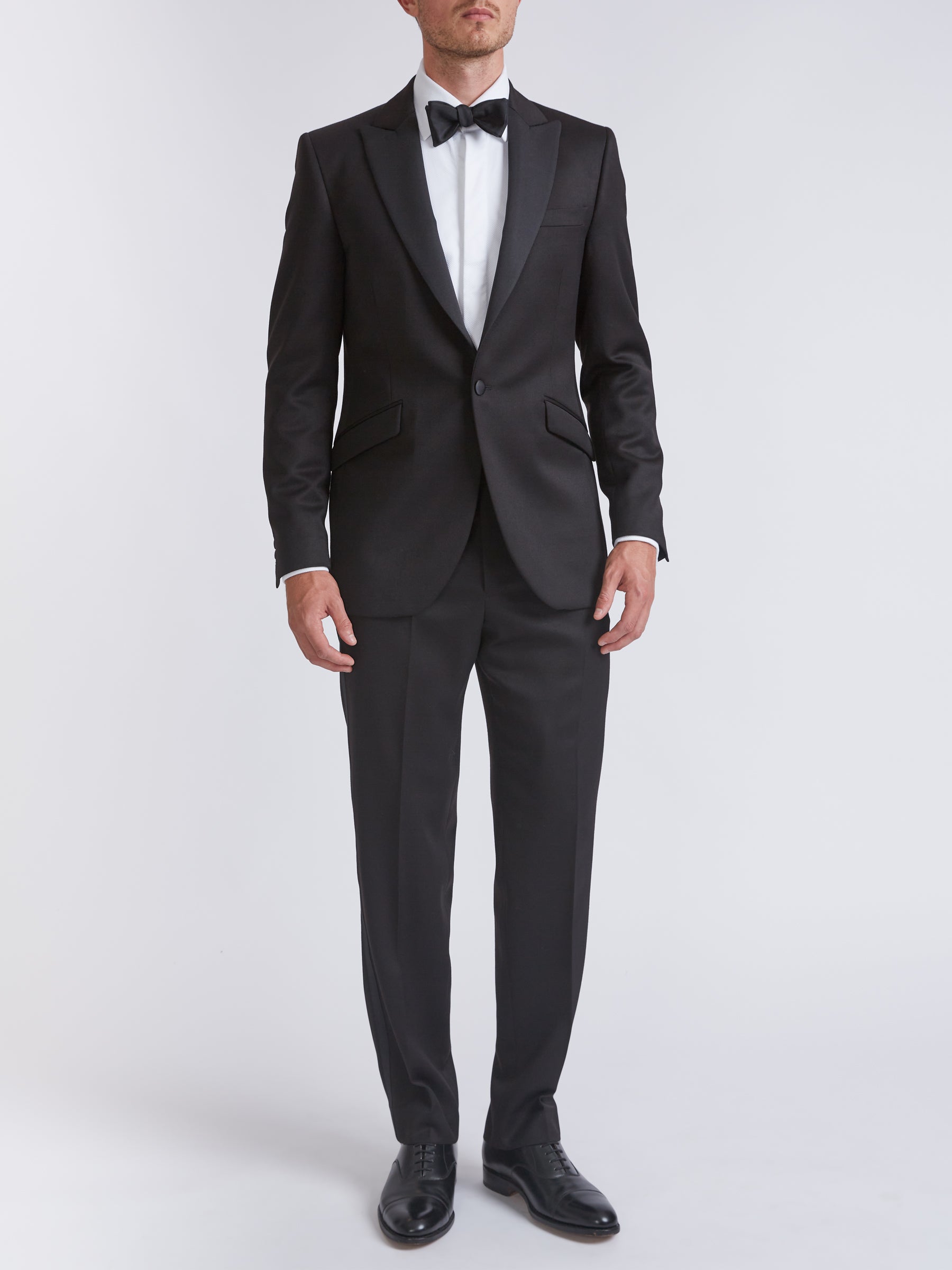 A black wool dinner suit with grosgrain silk peak lapels, shown on a model from the front.