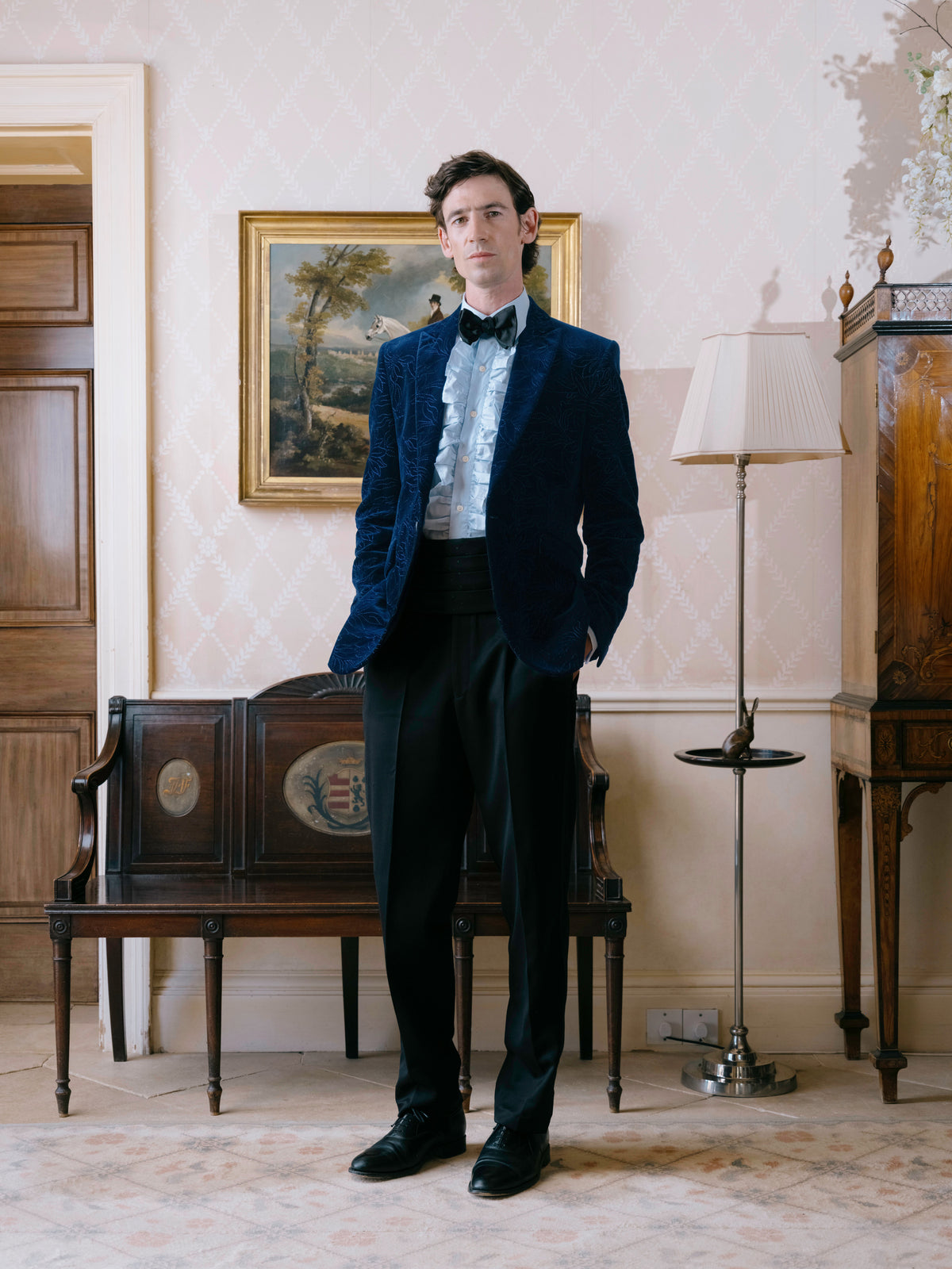 A navy embroidered velvet dinner jacket worn with a ruffled dress shirt and black bow tie