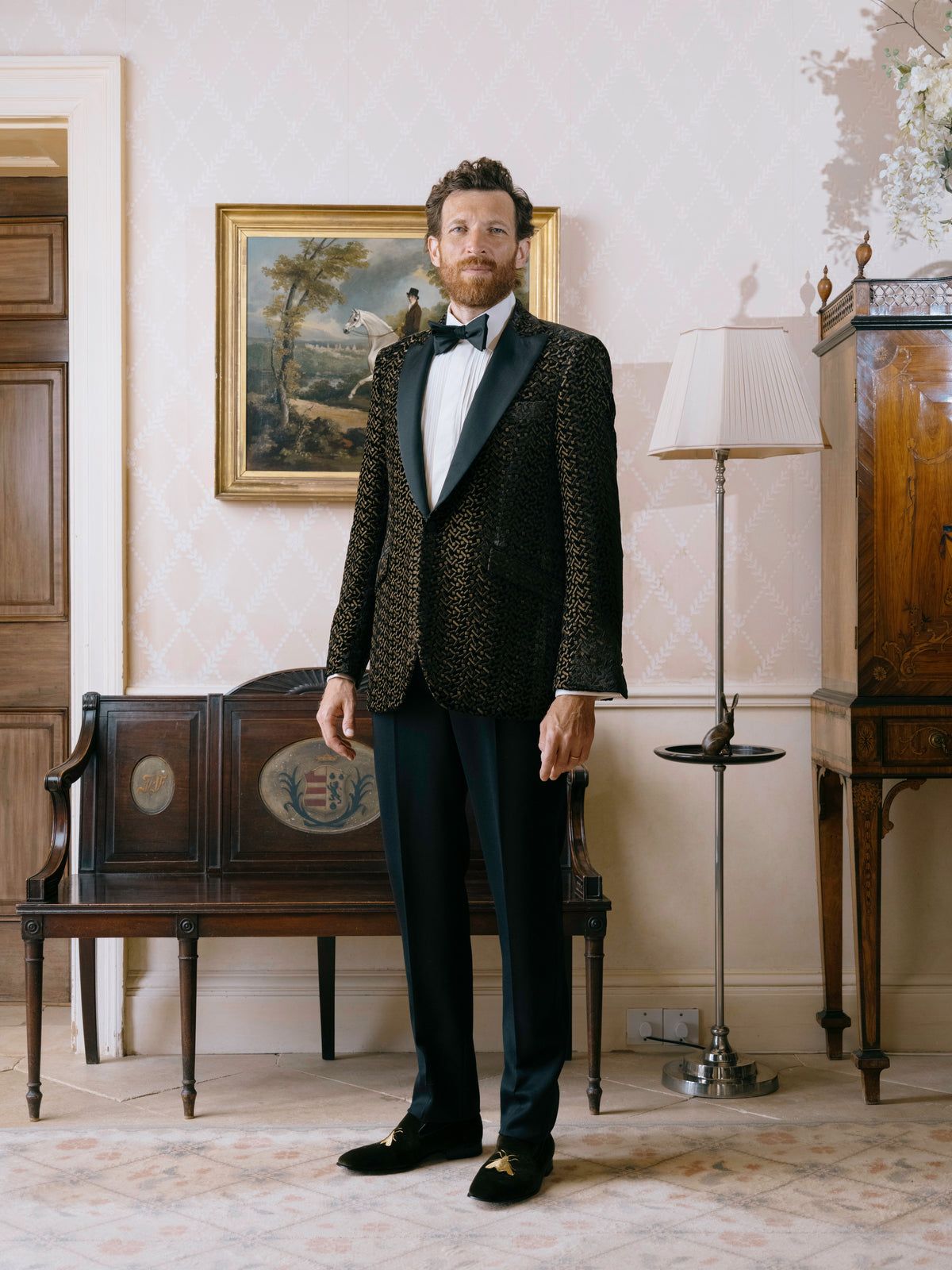 A black and gold jacquard dinner jacket worn with a black bow tie and velvet slippers