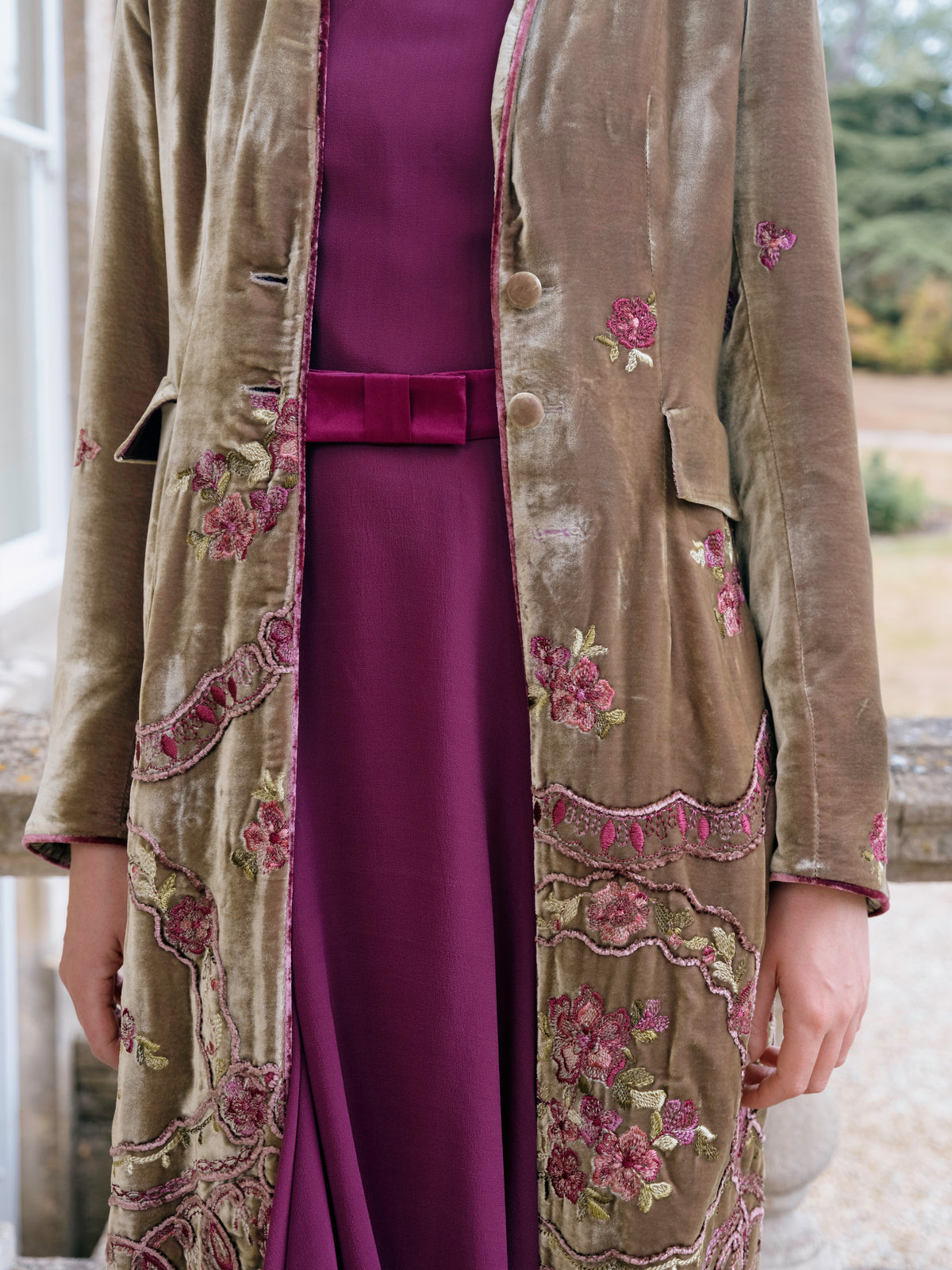 Close detail of the embroidery on an olive velvet coat over burgundy silk