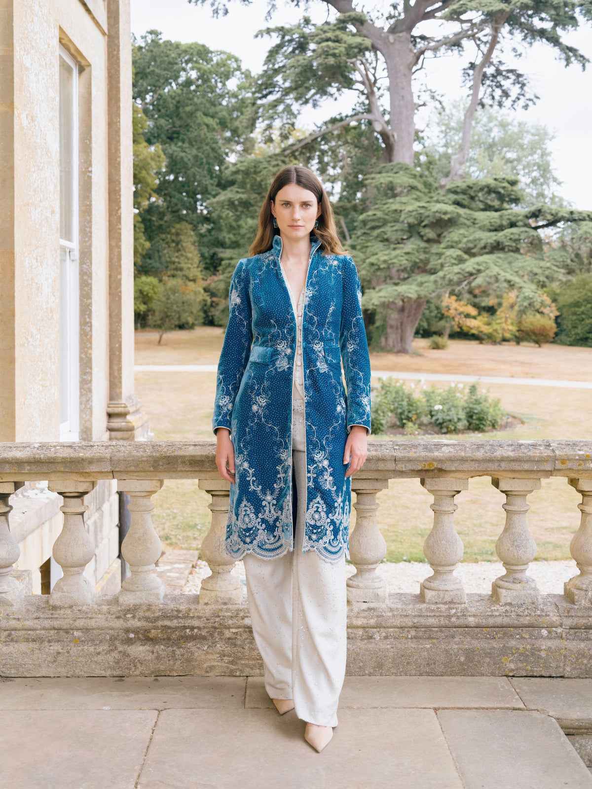Ivory trousers worn under a blue embroidered long coat
