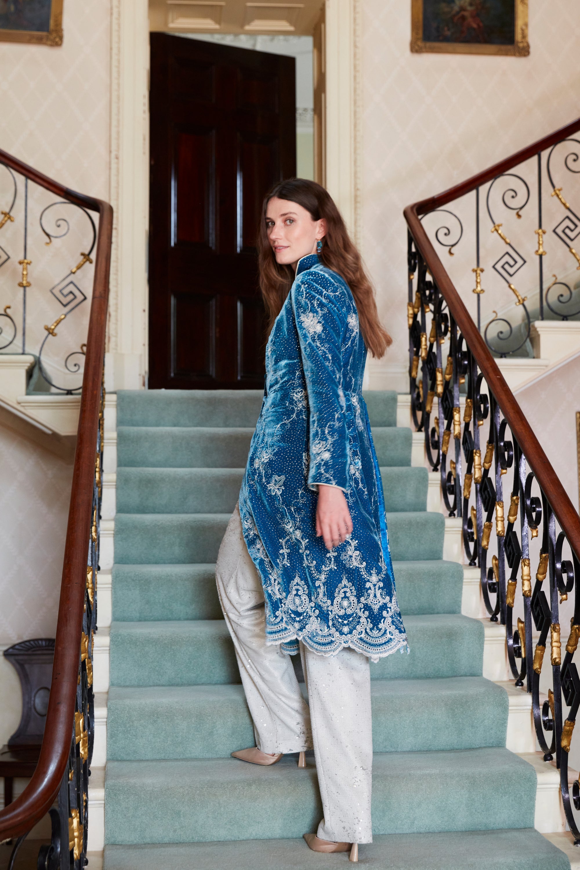 Favourbrook womenswear, Autumn/Winter '26: a model in a blue embroidered long coat on the stone staircase at Neston Park