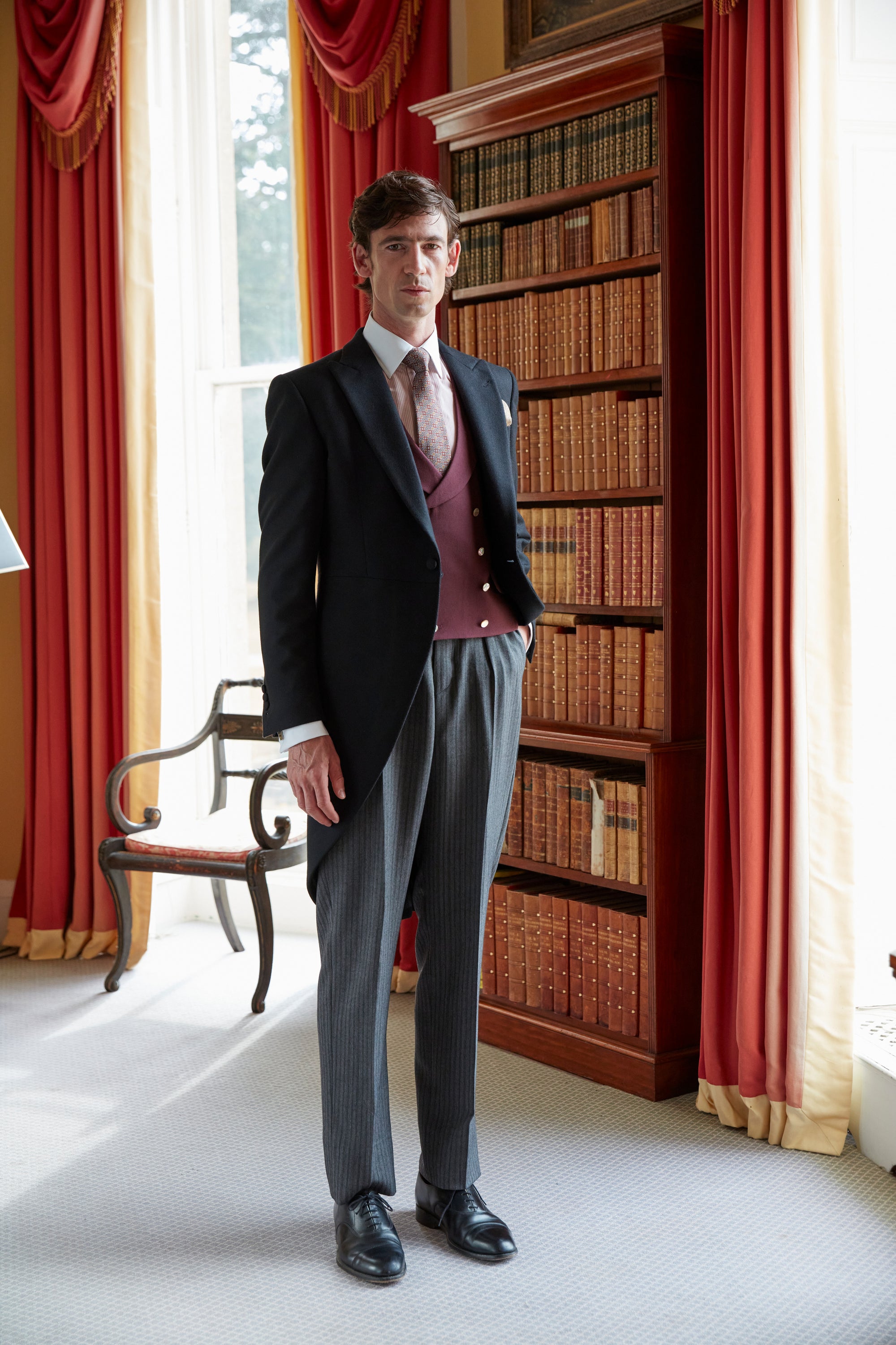Black morning coat with a burgundy double breasted waistcoat, grey striped trousers and a pink shirt and tie