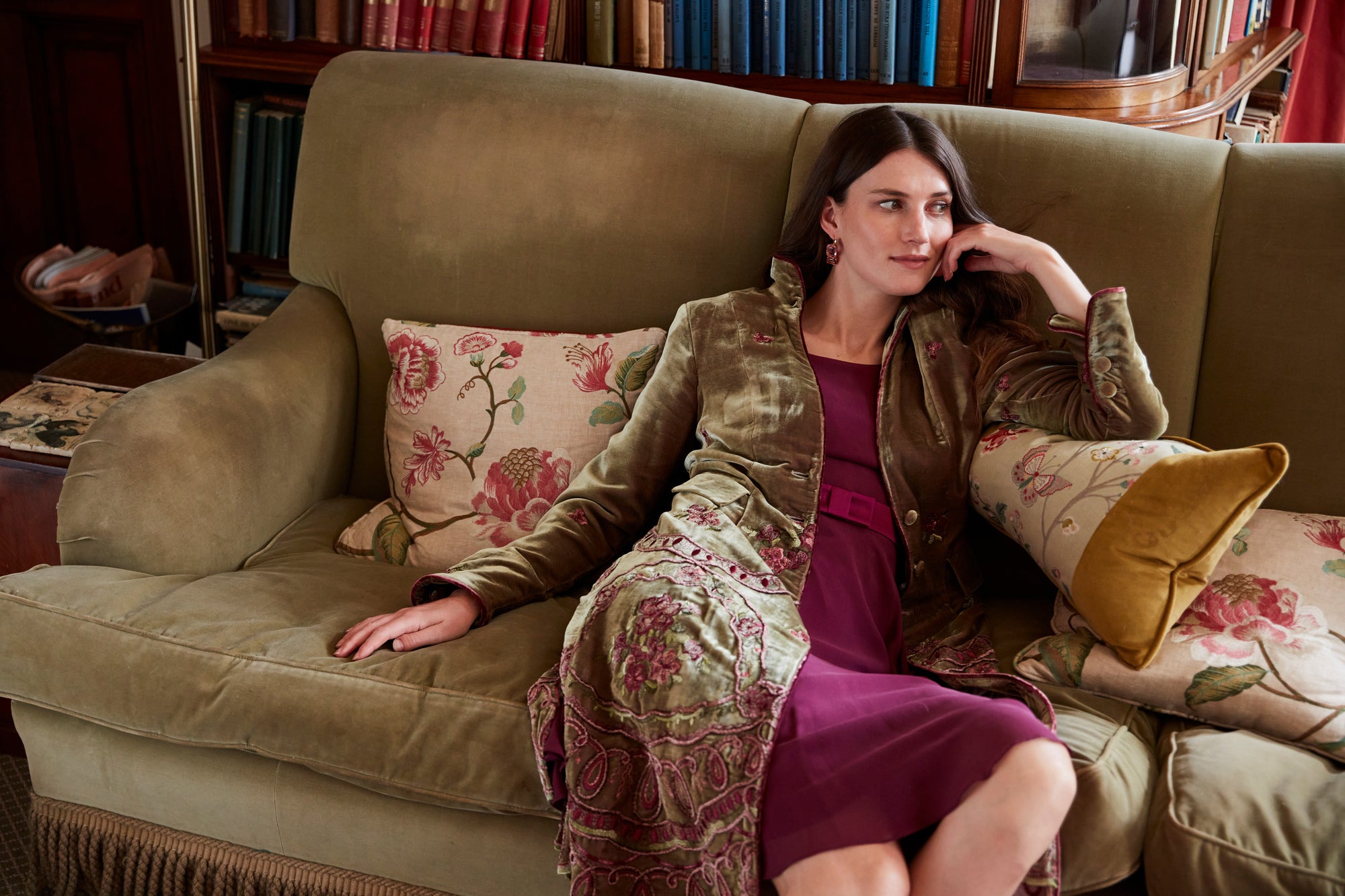 Favourbrook Autumn/Winter '26 womenswear, photographed at Neston Park: a model reclining on a green sofa in a gold and olive brocade jacket over a burgundy silk dress